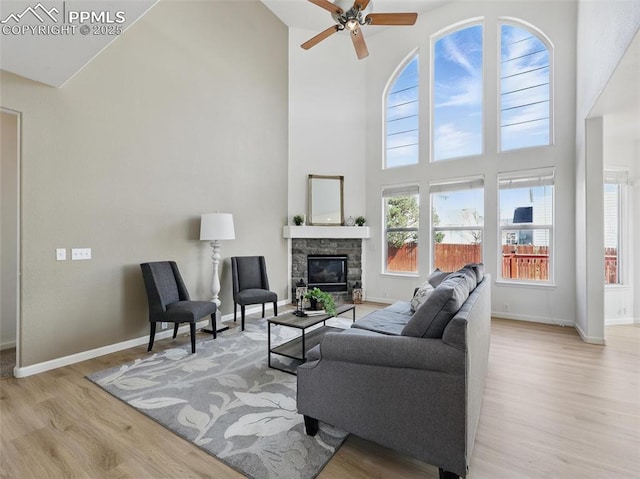 living area featuring a fireplace, high vaulted ceiling, a ceiling fan, baseboards, and wood finished floors