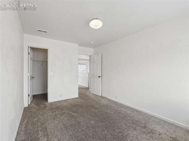 unfurnished bedroom featuring carpet floors, baseboards, a walk in closet, and visible vents
