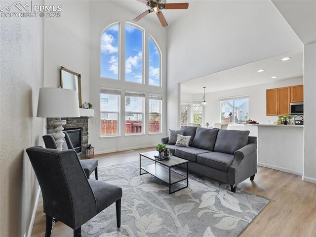 living room with ceiling fan, a high ceiling, a fireplace, light wood-style floors, and baseboards