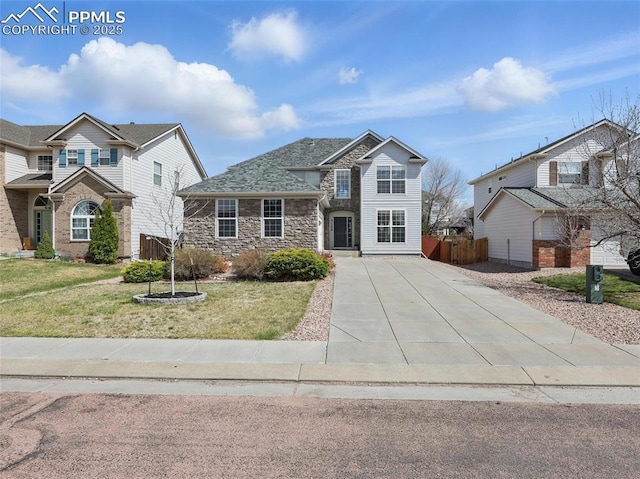 traditional home featuring fence, a front yard, driveway, and stone siding