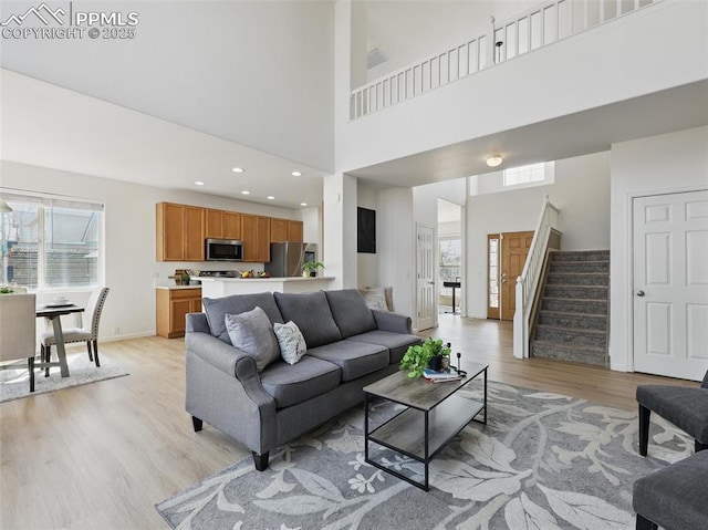 living room with stairway, baseboards, light wood finished floors, and a towering ceiling