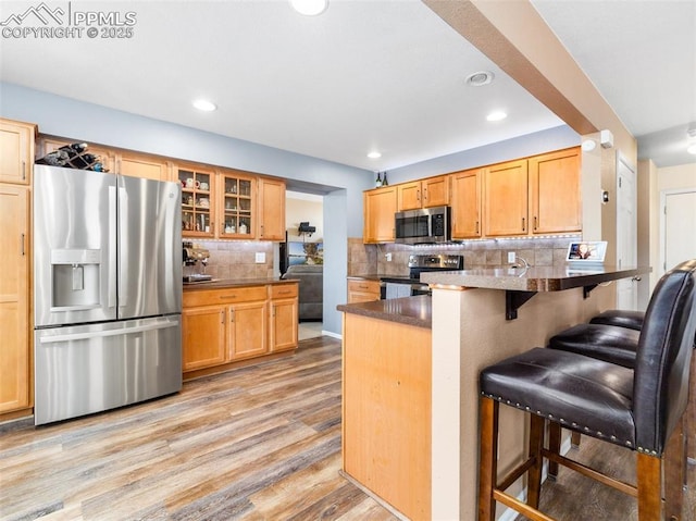 5346 Gentle Wind Rd, Colorado Springs, CO 80922 - kitchen featuring appliances with stainless steel finishes, a peninsula, a breakfast bar area, light wood-type flooring, and backsplash