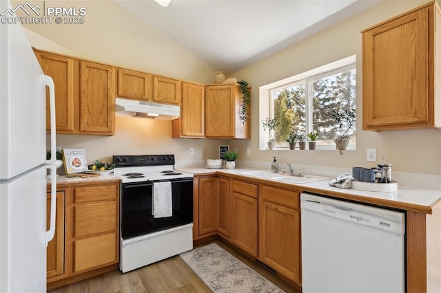 kitchen featuring white appliances, light wood-style floors, under cabinet range hood, a sink, and vaulted ceiling