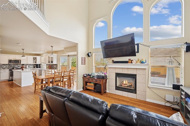 living room with recessed lighting, a tile fireplace, light wood finished floors, and a towering ceiling