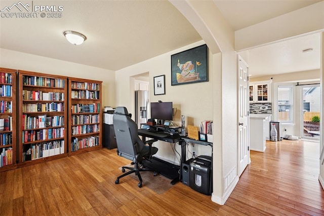 home office with arched walkways, baseboards, and wood finished floors