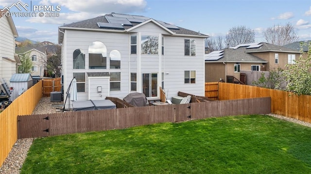 rear view of house featuring a yard, roof mounted solar panels, and a fenced backyard