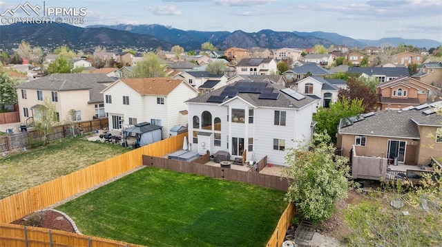back of property featuring a fenced backyard, a deck with mountain view, roof mounted solar panels, a lawn, and a residential view