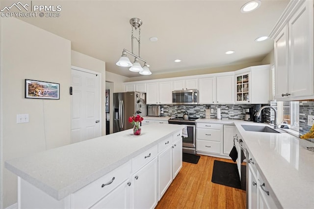 kitchen with a sink, light wood-style flooring, stainless steel appliances, white cabinetry, and tasteful backsplash