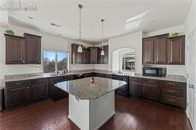 kitchen with dark brown cabinets, a sink, a kitchen island, visible vents, and black appliances