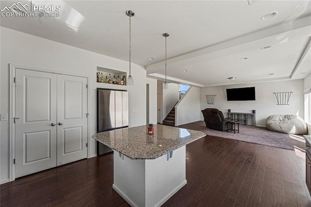 kitchen with stone countertops, freestanding refrigerator, a kitchen island, pendant lighting, and dark wood-style floors