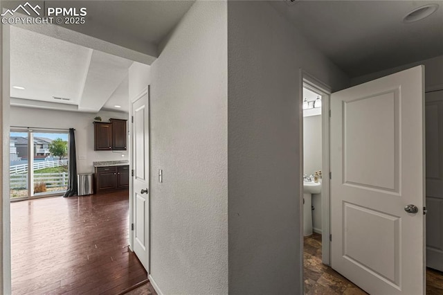 hall with dark wood-type flooring, a textured wall, and visible vents