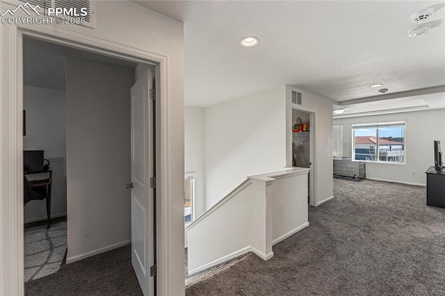 hall with a textured ceiling, an upstairs landing, dark carpet, and visible vents