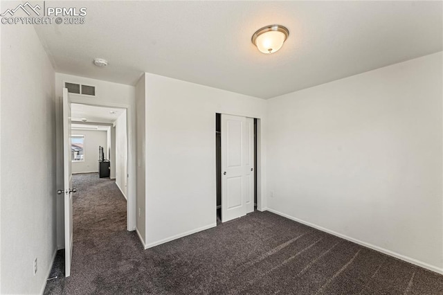 unfurnished bedroom featuring dark colored carpet, baseboards, visible vents, and a closet