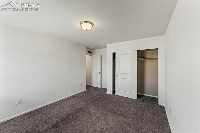 unfurnished bedroom with baseboards, visible vents, dark carpet, and a closet