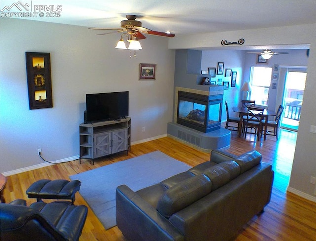 living room with baseboards, a ceiling fan, a tile fireplace, and wood finished floors