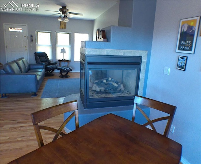 dining room featuring a ceiling fan, baseboards, wood finished floors, and a fireplace