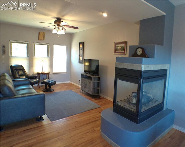 living room with a multi sided fireplace, a ceiling fan, baseboards, and wood finished floors