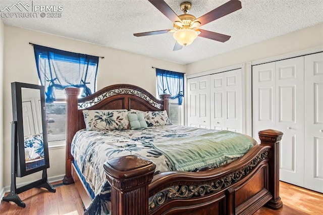 bedroom featuring multiple closets, wood finished floors, a textured ceiling, and ceiling fan