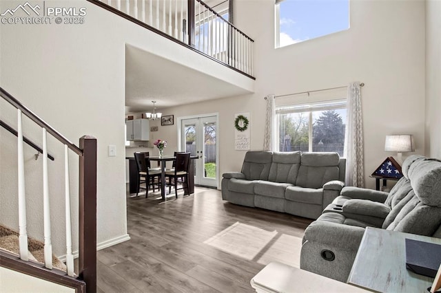 living room with stairs, wood finished floors, a towering ceiling, a chandelier, and french doors