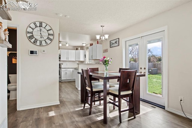 dining area featuring a textured ceiling, a chandelier, wood finished floors, baseboards, and french doors