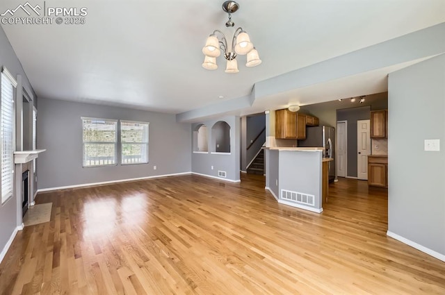 7824 Bengali Ln, Colorado Springs, CO 80923 - unfurnished living room with a notable chandelier, visible vents, a fireplace with flush hearth, and light wood-type flooring