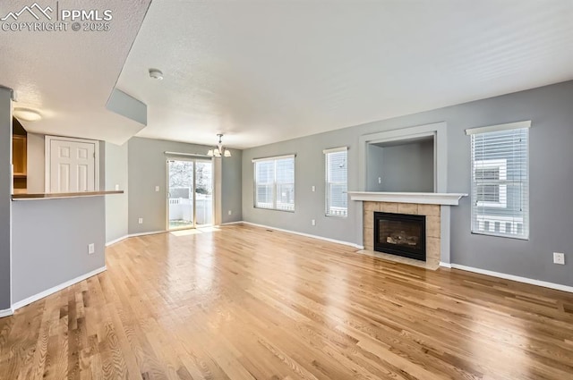 7824 Bengali Ln, Colorado Springs, CO 80923 - unfurnished living room featuring light wood-style floors, baseboards, a tiled fireplace, and a chandelier