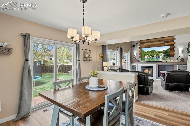dining area featuring a chandelier, a glass covered fireplace, light wood-type flooring, and baseboards