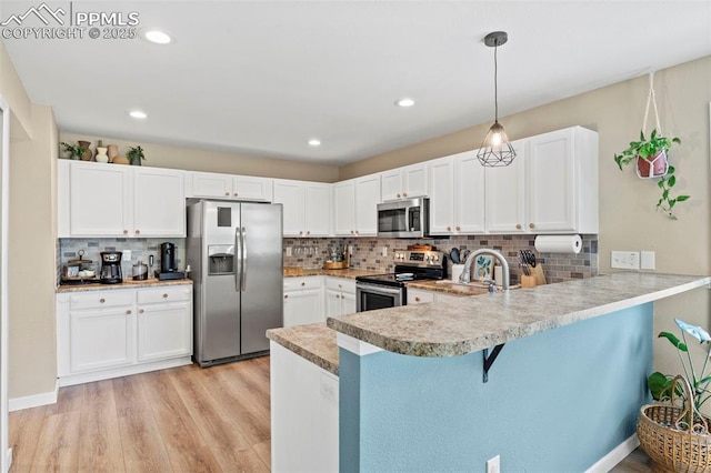 kitchen featuring appliances with stainless steel finishes, a peninsula, decorative backsplash, light wood finished floors, and a kitchen breakfast bar