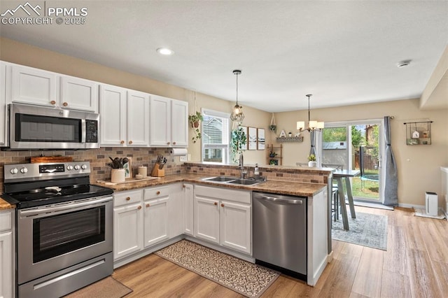 kitchen with stainless steel appliances, a sink, white cabinetry, a peninsula, and light wood-style flooring