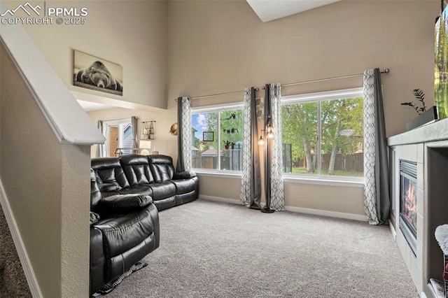 living room with a glass covered fireplace, carpet flooring, baseboards, and a high ceiling