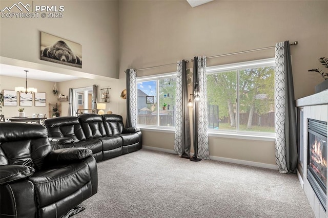 living area featuring carpet flooring, a chandelier, baseboards, a glass covered fireplace, and a towering ceiling