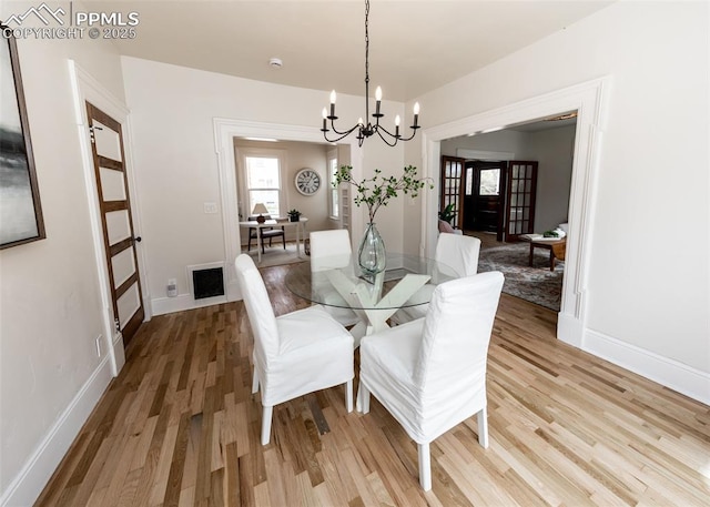 dining room with baseboards, light wood finished floors, and a notable chandelier