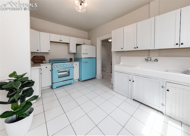 kitchen featuring light countertops, white cabinets, freestanding refrigerator, electric stove, and light tile patterned flooring