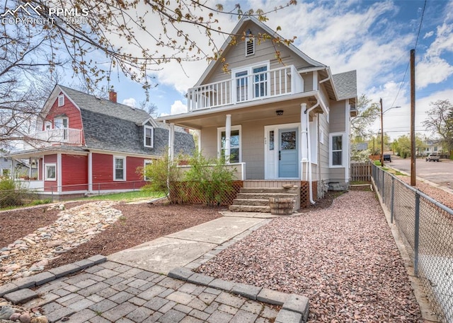 victorian house with a porch, fence, a balcony, and roof with shingles