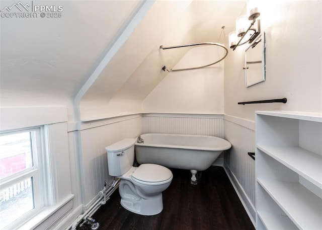 bathroom with toilet, wood finished floors, a soaking tub, and a wainscoted wall