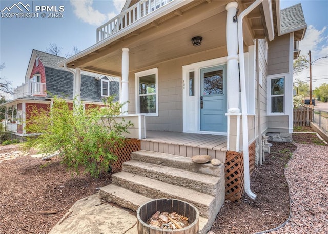 entrance to property featuring a porch, roof with shingles, and fence