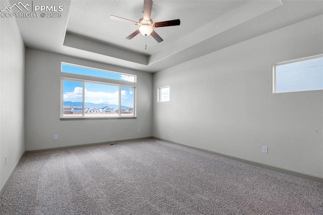 carpeted spare room with a ceiling fan, baseboards, and a tray ceiling
