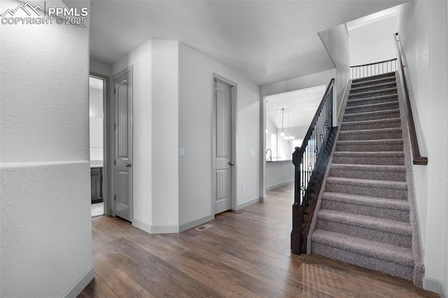 stairway featuring baseboards, a chandelier, and wood finished floors