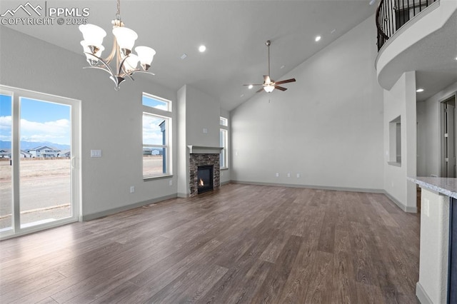 unfurnished living room with high vaulted ceiling, a stone fireplace, ceiling fan with notable chandelier, baseboards, and wood finished floors