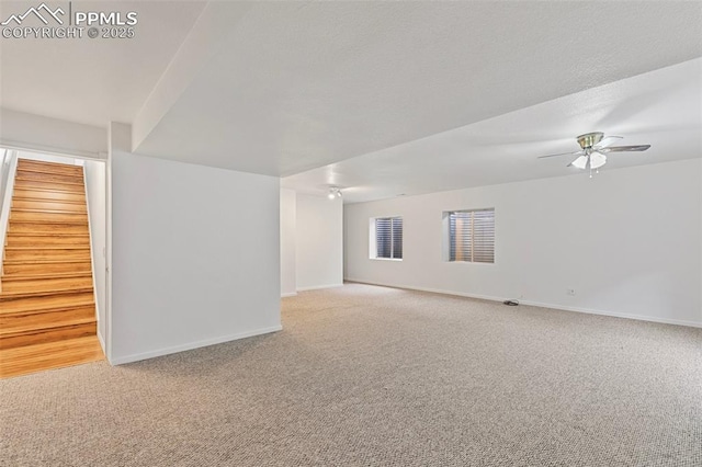 carpeted empty room featuring baseboards, stairway, and a ceiling fan