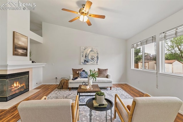 living room featuring lofted ceiling, a tiled fireplace, ceiling fan, baseboards, and wood finished floors