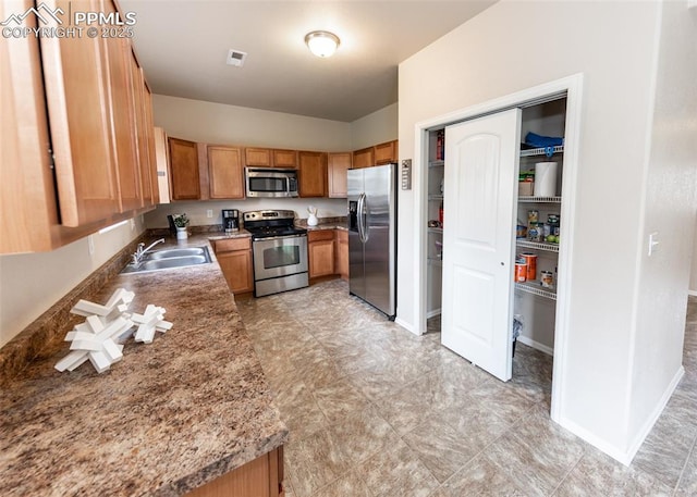 kitchen featuring visible vents, baseboards, brown cabinets, a sink, and appliances with stainless steel finishes