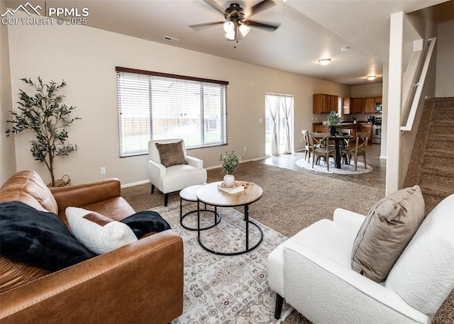 living area featuring visible vents, carpet floors, stairs, baseboards, and a ceiling fan