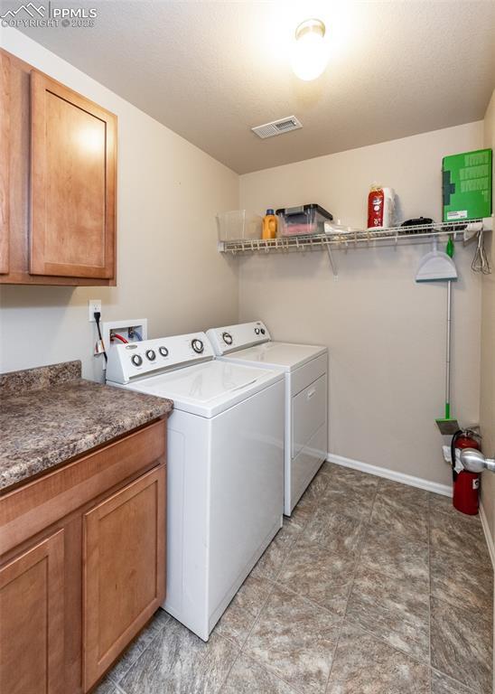 clothes washing area featuring baseboards, visible vents, cabinet space, and washing machine and clothes dryer