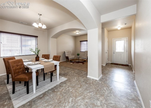 dining area featuring baseboards, arched walkways, a chandelier, and a wealth of natural light