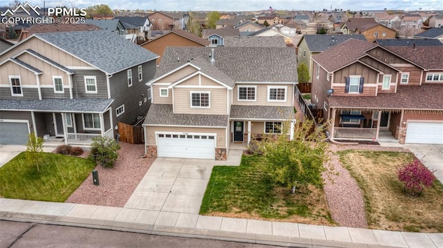 traditional home featuring a porch, roof with shingles, a residential view, concrete driveway, and stone siding