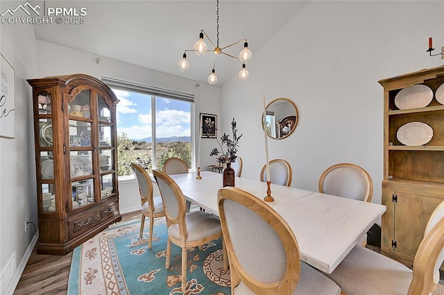 dining room featuring wood finished floors, baseboards, a mountain view, a notable chandelier, and vaulted ceiling