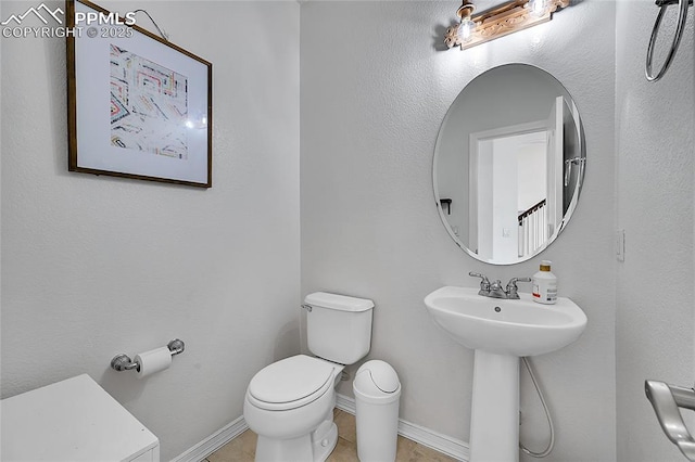 half bath with toilet, baseboards, and tile patterned floors