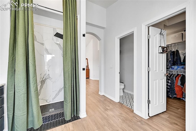 corridor with light wood-style floors, arched walkways, and baseboards