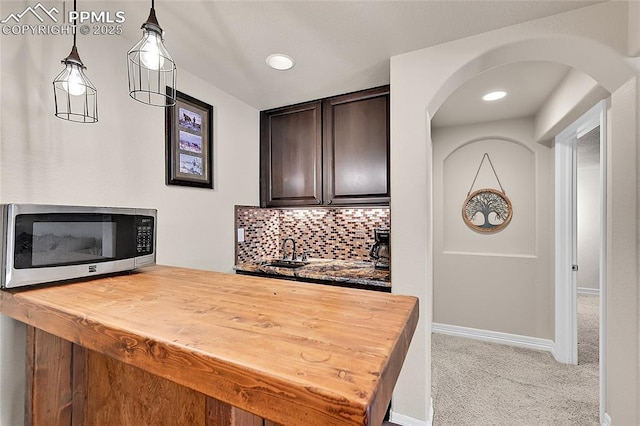 interior space featuring dark brown cabinetry, arched walkways, stainless steel microwave, butcher block counters, and light carpet